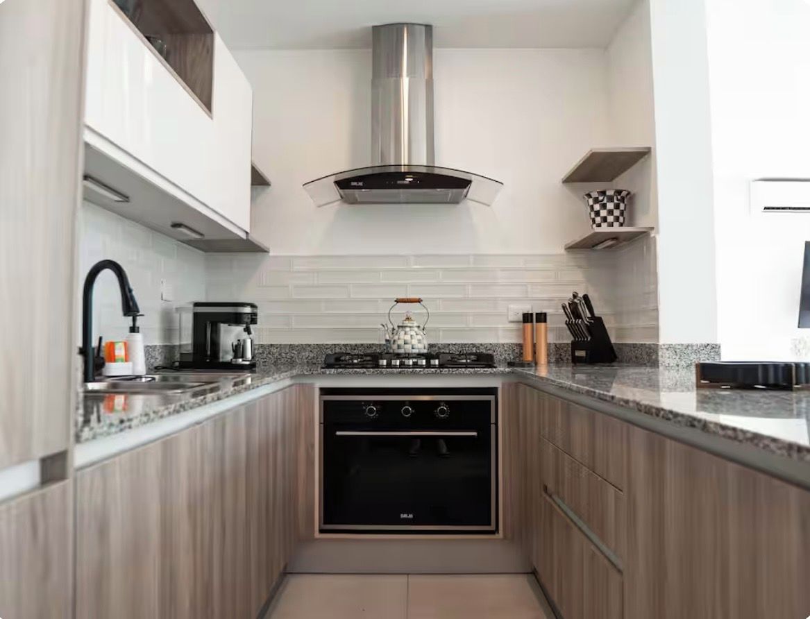 A modern kitchen with a built-in oven, stainless steel range hood, and a granite countertop.