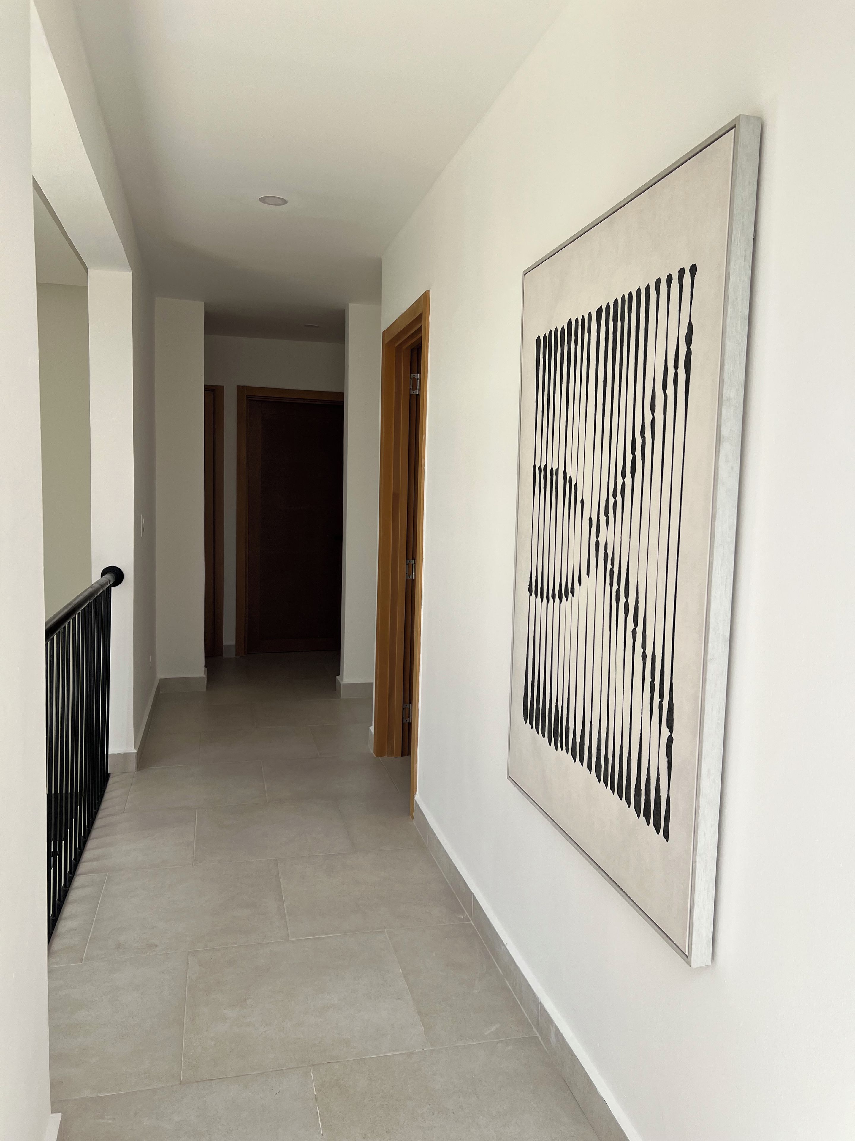 Um corredor com piso de azulejos, corrimão preto e uma grande pintura abstrata na parede.