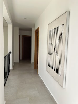 Un pasillo con piso de baldosas, barandal negro y un cuadro abstracto grande en la pared.