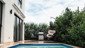 Une piscine avec un espace patio comprenant une chaise et une table.