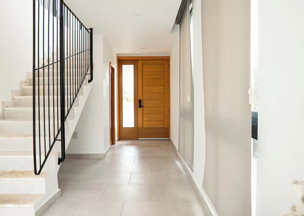 A hallway with a staircase, a wooden door, and a light-colored floor.