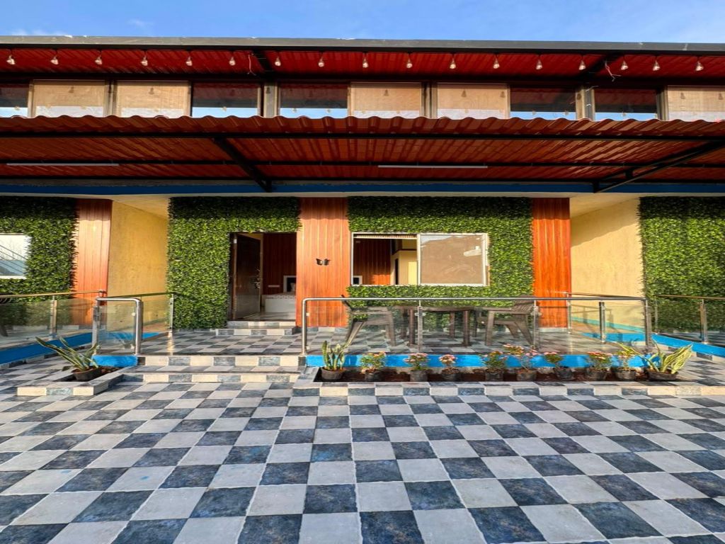 A hotel entrance with a checkered floor, a covered walkway, and a green wall with plants.