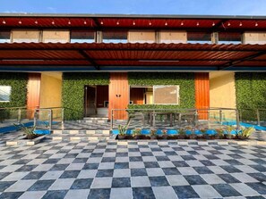 A hotel entrance with a checkered floor, a covered walkway, and a green wall with plants.