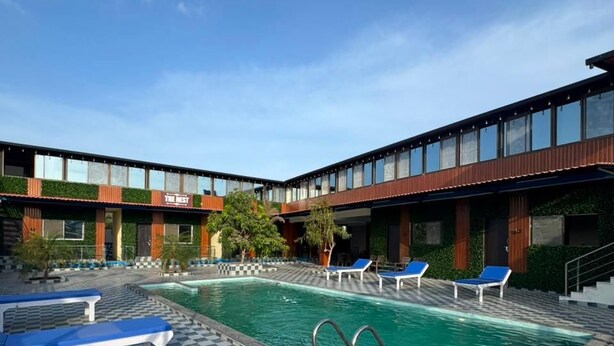 Zona de piscina de hotel con suelo a cuadros, sillones de descanso y un edificio con un cartel que dice 'THE BEST'.