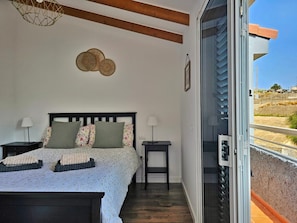 A bedroom with a bed, bedside tables, a wall-mounted decorative item, and a sliding glass door leading to an outdoor area. - Hoya del Viejo Duplex - Laaldeabnb (CN)