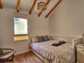 Een slaapkamer met een bed, een stoel, een nachtkastje en een raam met jaloezieën.