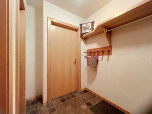 Ein Flur mit einer Holztür, einem Kachelboden und einem an der Wand befestigten Regal mit einem Korb.