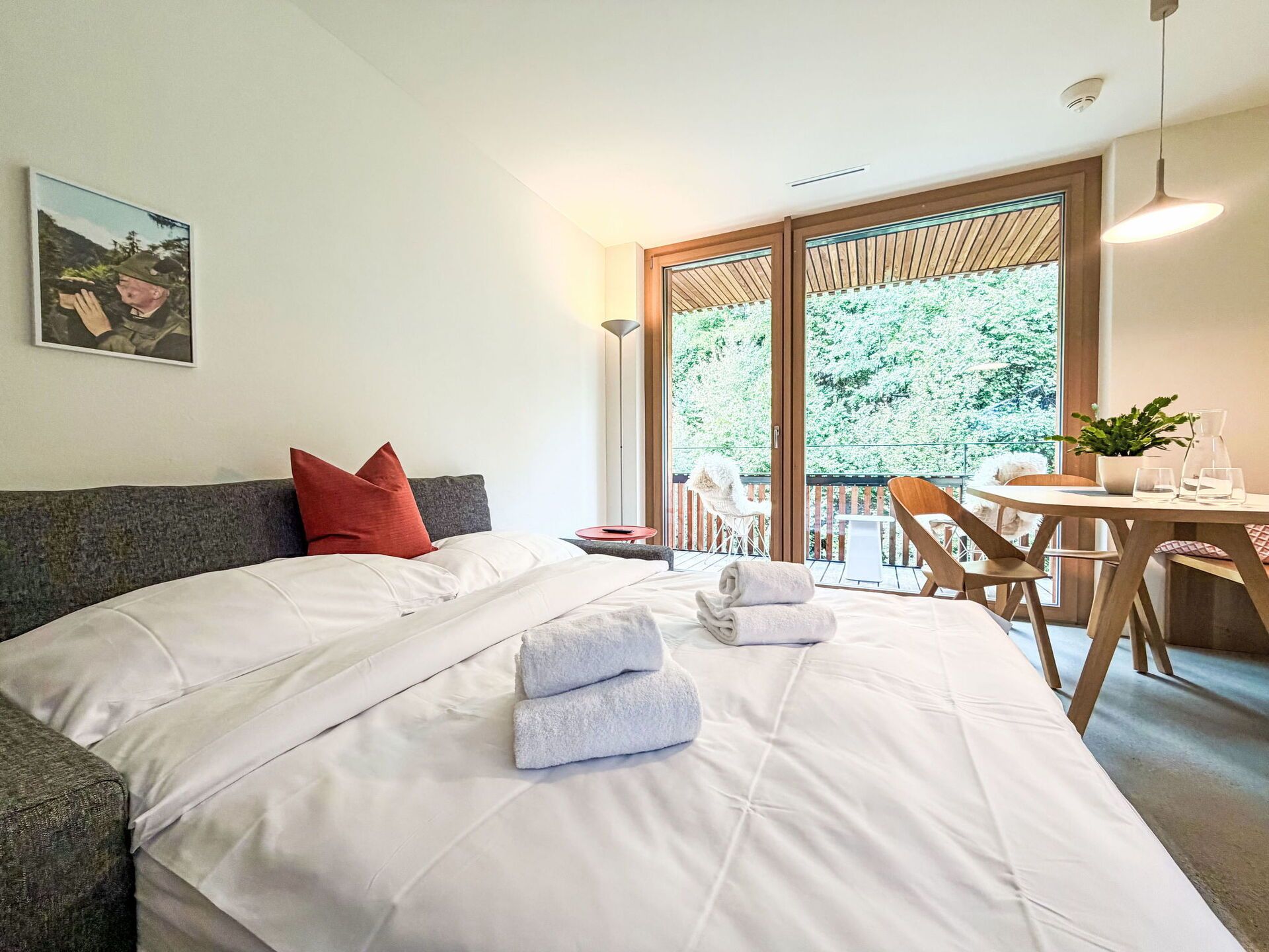 Ein Hotelzimmer mit Bett, Esstisch und Balkon mit Blick auf Bäume.