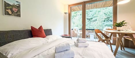 Una camera d'albergo con un letto, un tavolo da pranzo e un balcone affacciato sugli alberi.
