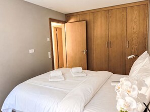 Ein Hotelzimmer mit einem Doppelbett, einem Holzschrank und einer Tür zu einem anderen Raum.