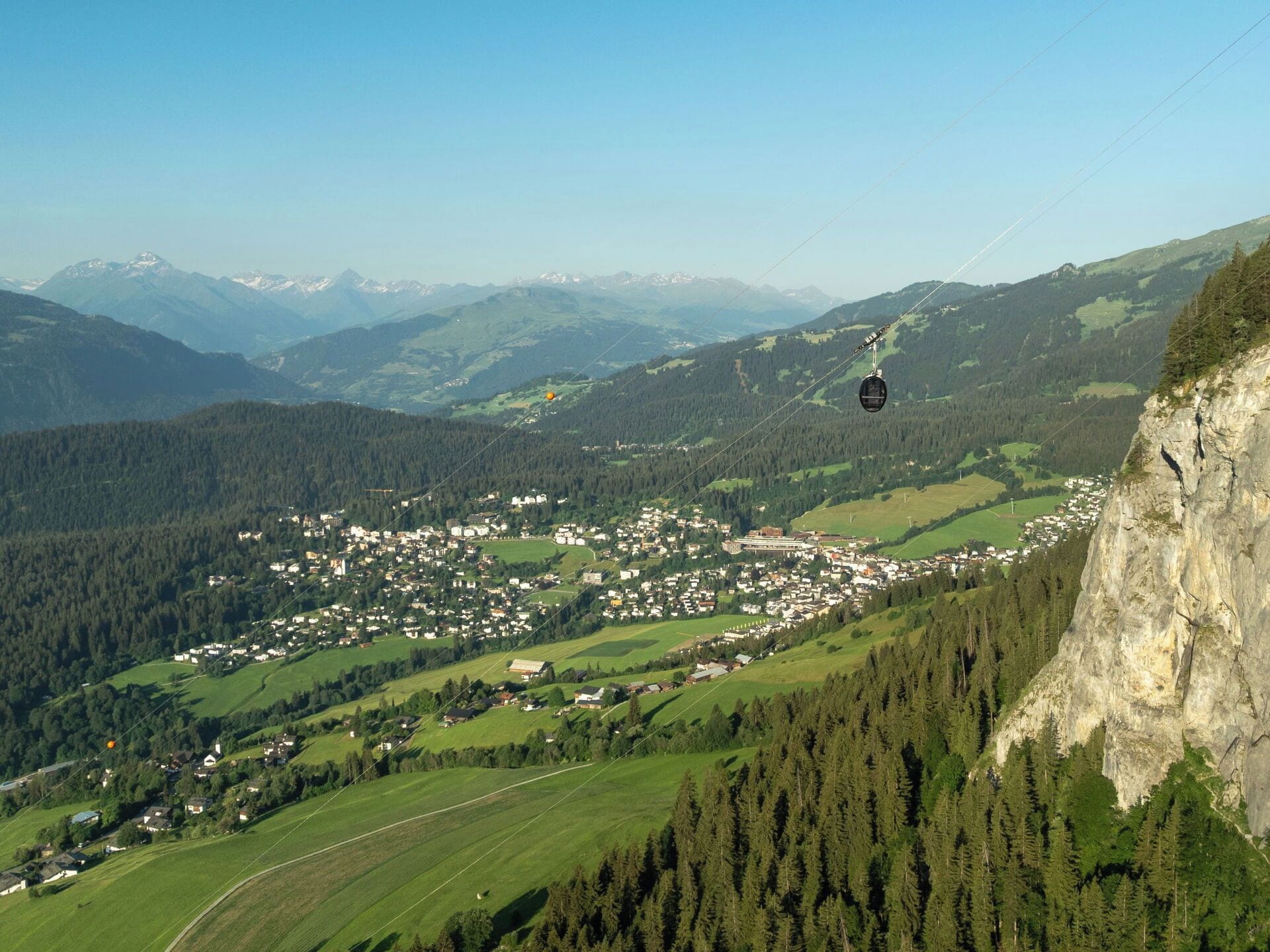 Eine Seilbahn über einer Stadt, umgeben von Bergen und Wäldern.