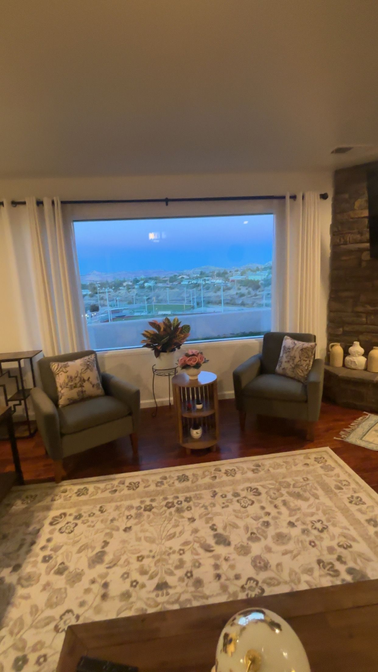 A living room with two sofas, a coffee table, a rug, and a view of a distant landscape through a large window.