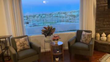 A living room with two sofas, a coffee table, a rug, and a view of a distant landscape through a large window.