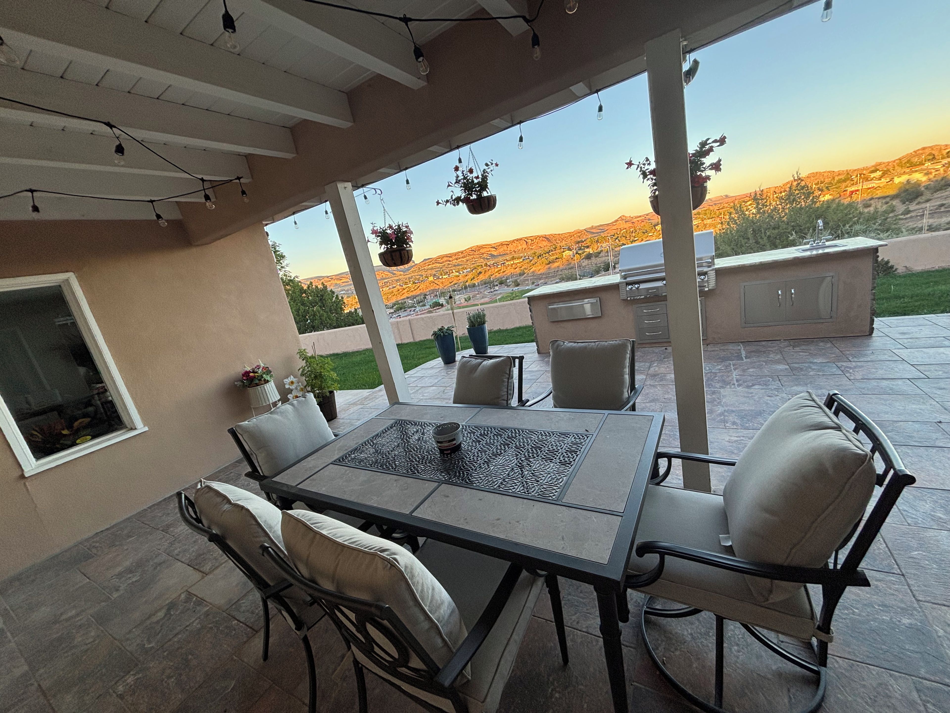 Une terrasse extérieure avec une table et des chaises, un barbecue et des plantes suspendues.