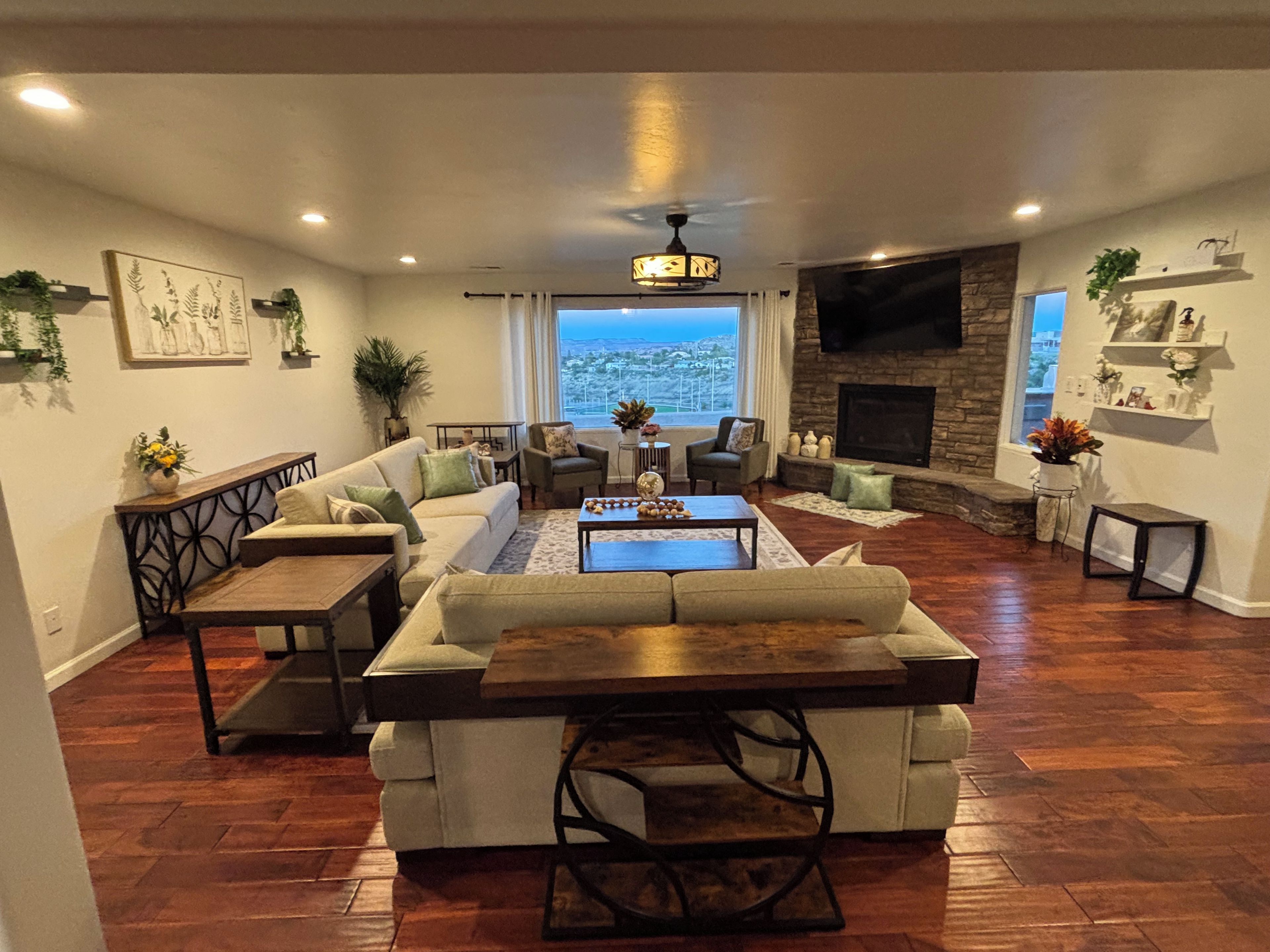 A spacious living room with a sectional sofa, a coffee table, and a fireplace. There is a large window providing a view of the outdoors.