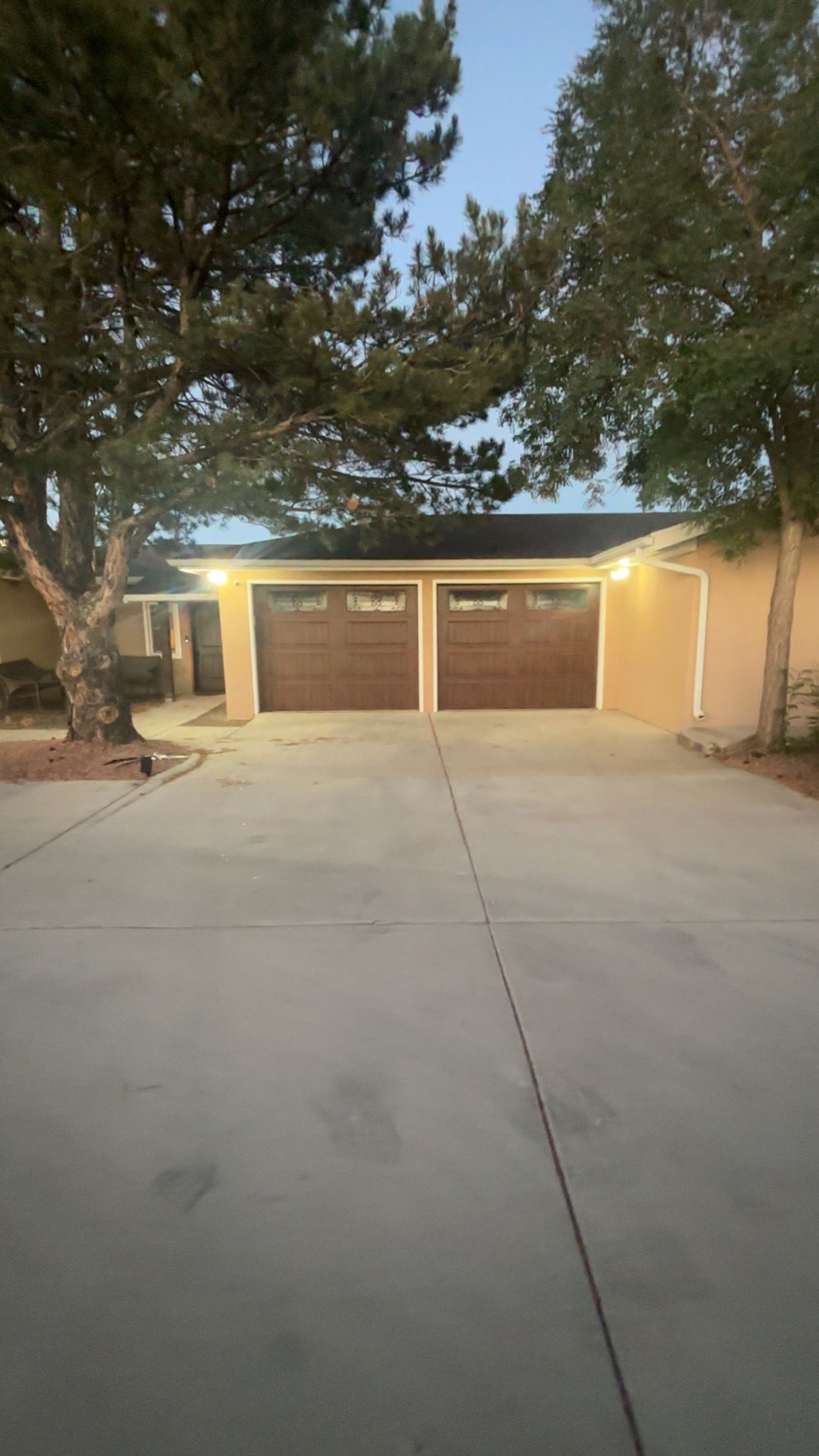 Un garage attenant à une maison, avec deux portes, une allée et un arbre.