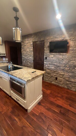 A kitchen with a stone wall, wooden flooring, a built-in oven, and a stone fireplace.