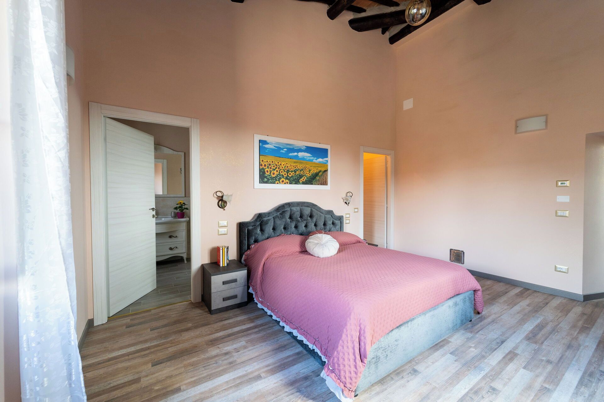 Une chambre à coucher comprenant un lit, des tables de chevet, une commode, un tableau et une porte donnant sur une autre pièce.