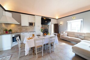A modern kitchen with white cabinetry, a dining table set for four, and a living area with a sofa and a TV. - Stunning private villa with WIFI, A/C, private pool, TV, veranda, panoramic view, close to Cortona (Camucia-monsigliolo)