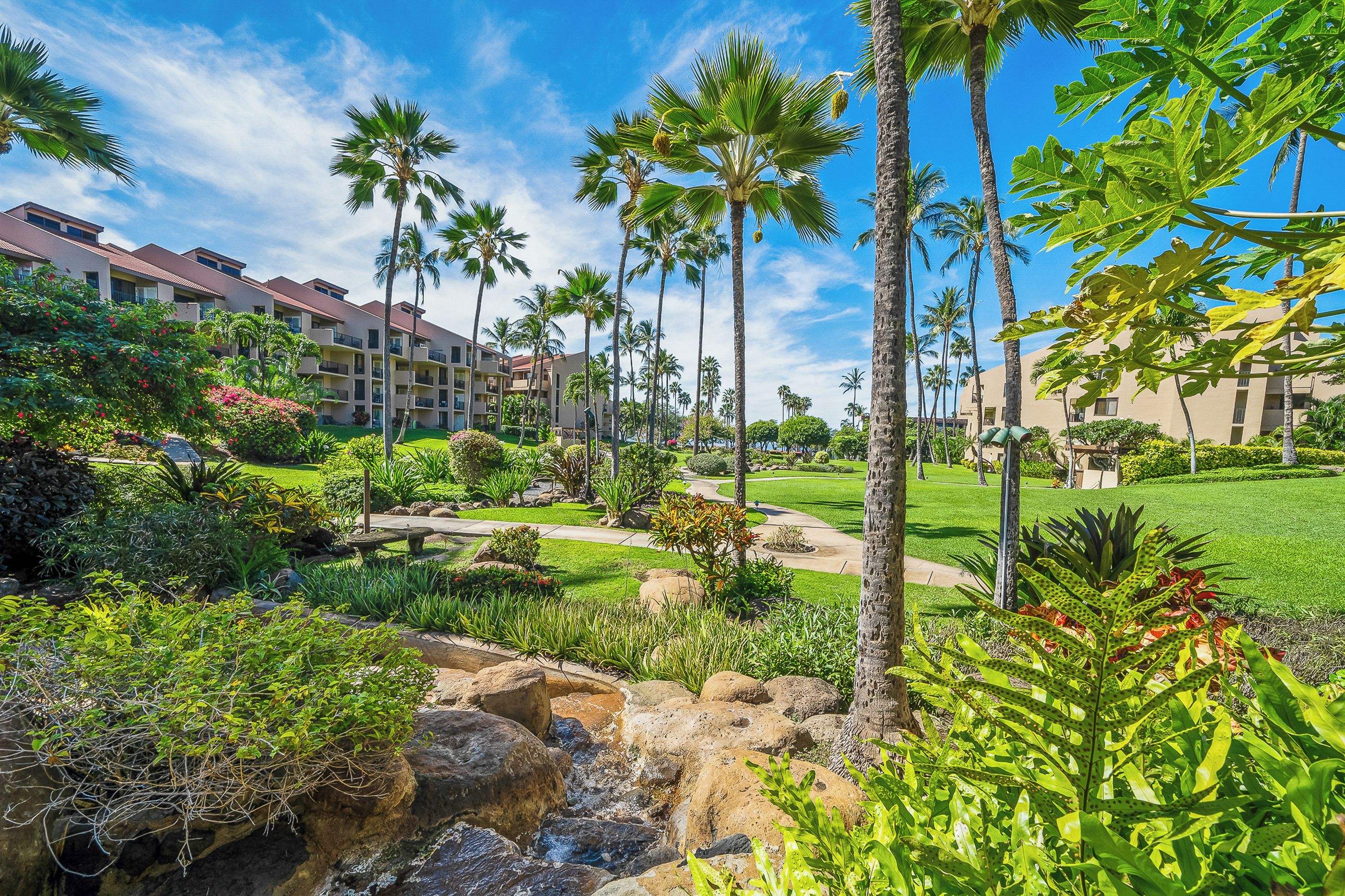 A resort with a well-maintained garden, palm trees, and a clear blue sky.