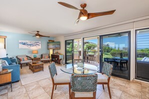 A spacious living area with a glass-top dining table surrounded by woven chairs, a ceiling fan, and artwork on the walls. - Remodeled Ocean View | Wailea Ekolu 703 (Wailea)