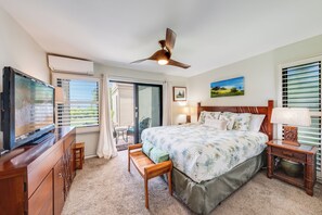 A bedroom with a bed, a desk, a chair, a ceiling fan, and a window with blinds. - Remodeled Ocean View | Wailea Ekolu 703 (Wailea)