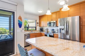 A modern kitchen with wooden cabinets, stainless steel appliances, and a large island. - Remodeled Ocean View | Wailea Ekolu 703 (Wailea)
