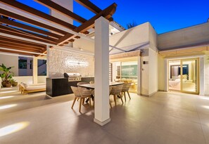 Ein Terrassenbereich im Freien mit Grill, Esstisch und Stühlen.