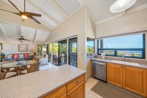 A modern kitchen with a large window, a dining area with a glass table, and a ceiling fan. - Ocean View Wailea 2bd I Wailea Ekolu 702 (Kihei)