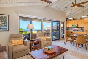 A spacious living area with a view of the ocean, a dining area with wicker chairs, and a kitchen with wooden cabinets. - Ocean View Wailea 2bd I Wailea Ekolu 702 (Kihei)