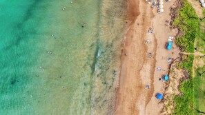 Vista aèria d'una platja amb aigua cristal·lina, sorra daurada i diverses papereres.