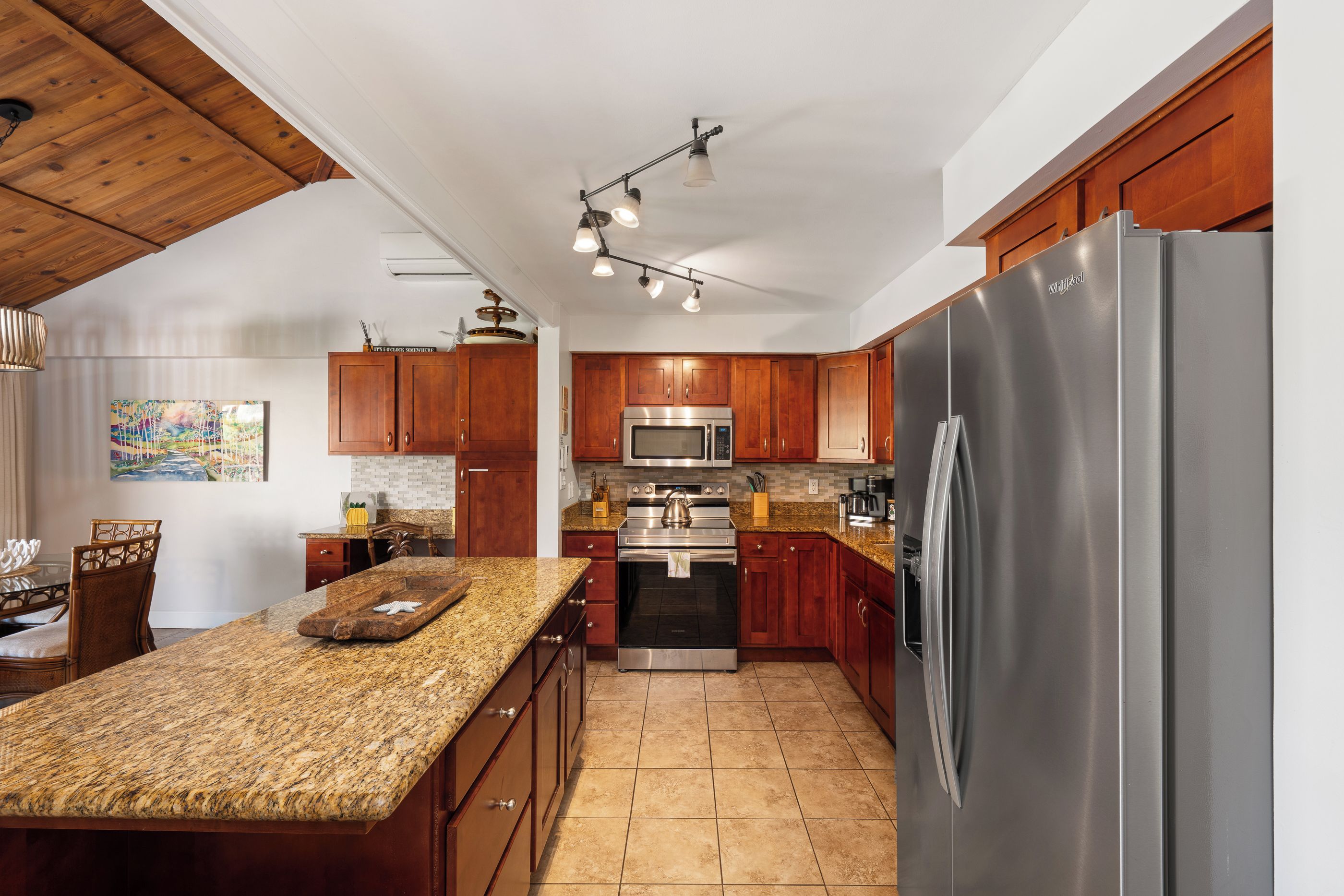 A kitchen with wooden cabinets, a granite countertop, stainless steel appliances, and a dining area with a chair and table.