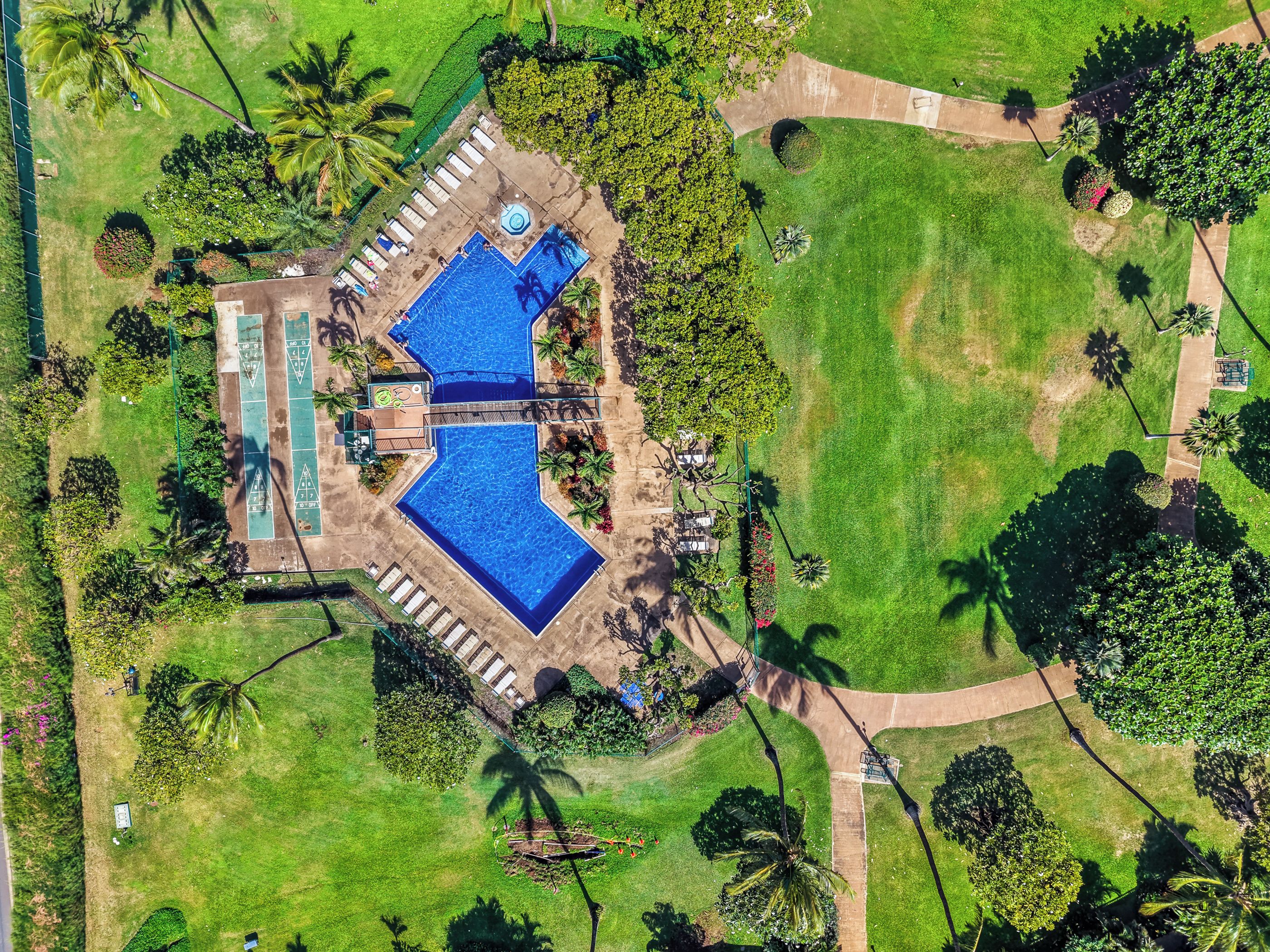 An aerial view of a resort with a large swimming pool, multiple lounge areas, and well-maintained gardens.