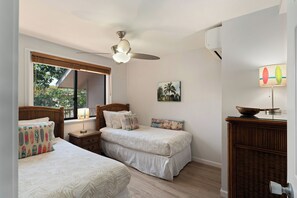 Ein Schlafzimmer mit zwei Betten, einem Deckenventilator, einem Fenster mit Blick auf Grünflächen und einer wandmontierten Klimaanlage.