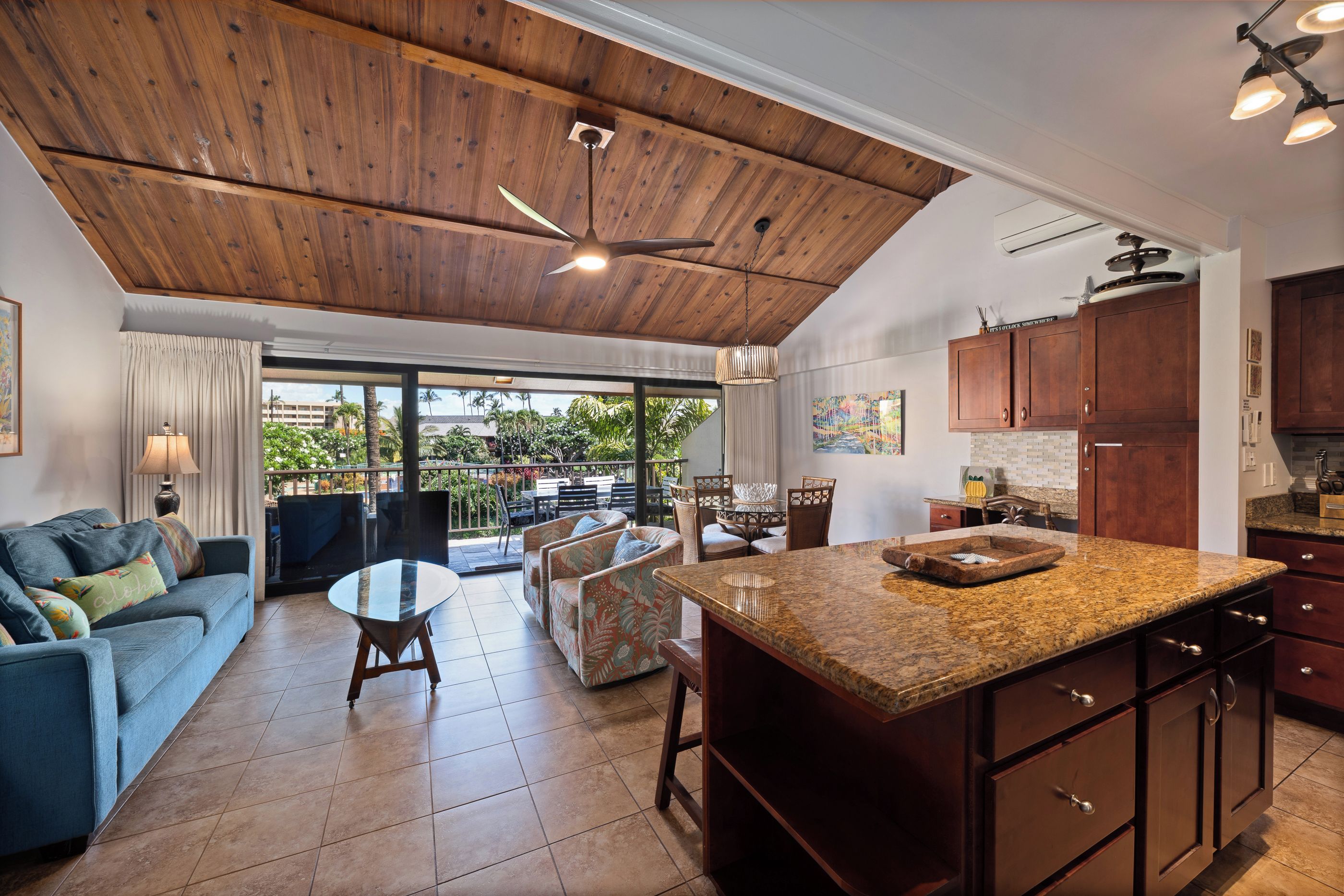 A spacious living area with a large wooden ceiling, a kitchen with dark wooden cabinets, and a dining area with a glass table.