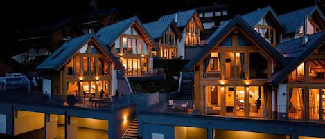 A cluster of log cabins with multiple levels and large windows, surrounded by a forested landscape.