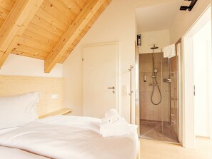 A bedroom with a wooden ceiling, a bed with white bedding, and a glass-enclosed shower area. - Cabin in Niederwolz With Sauna (Oberwölz)