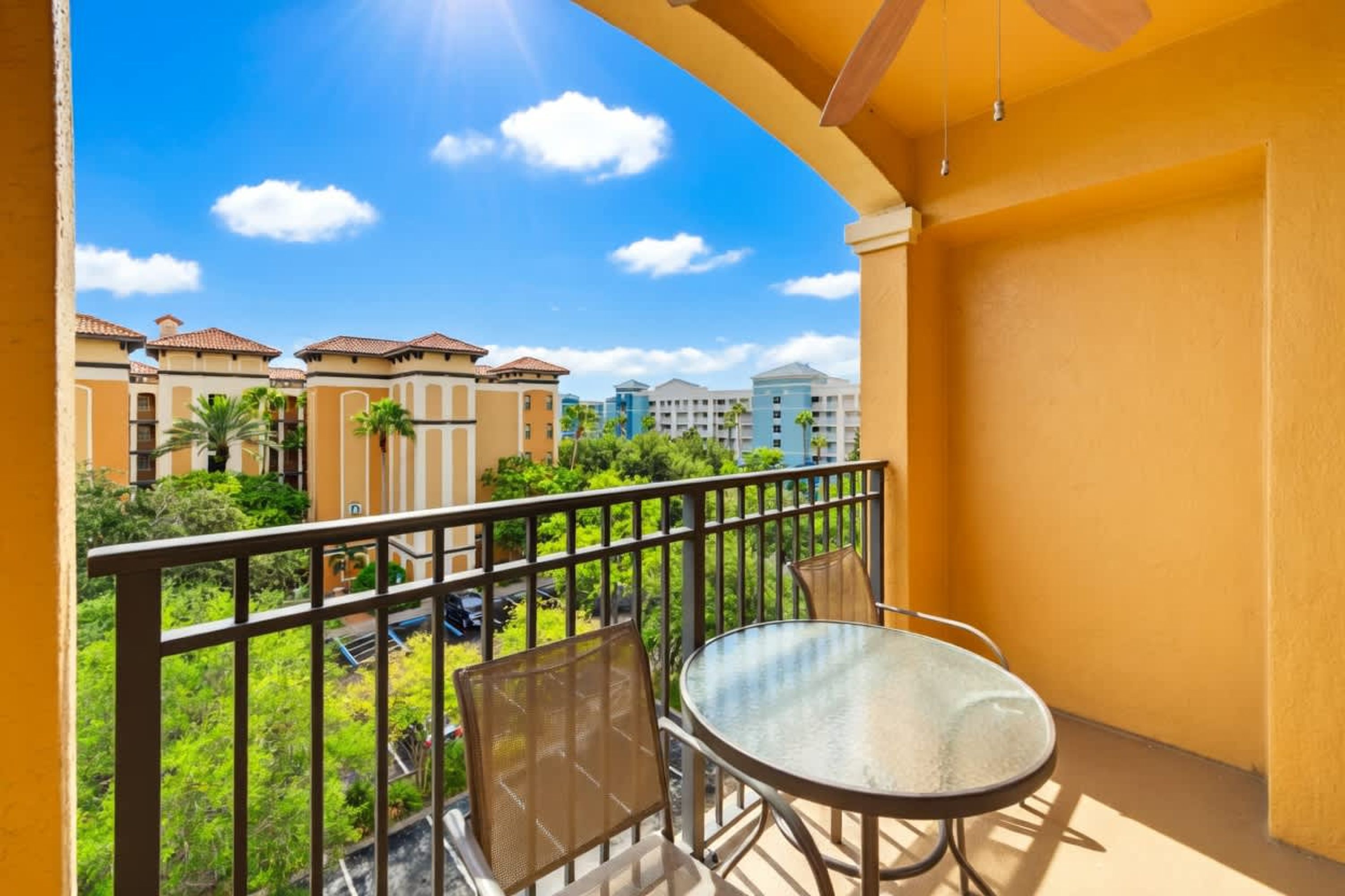 Ein Balkon mit Glastisch und Stuhl, mit Blick auf ein Wohngebiet mit Gebäuden und Grünflächen.