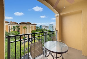 A balcony with a table and chairs, a view of a residential area with buildings and palm trees. - Magical 2BR Disney Condo - Free Resort Access (Orlando)