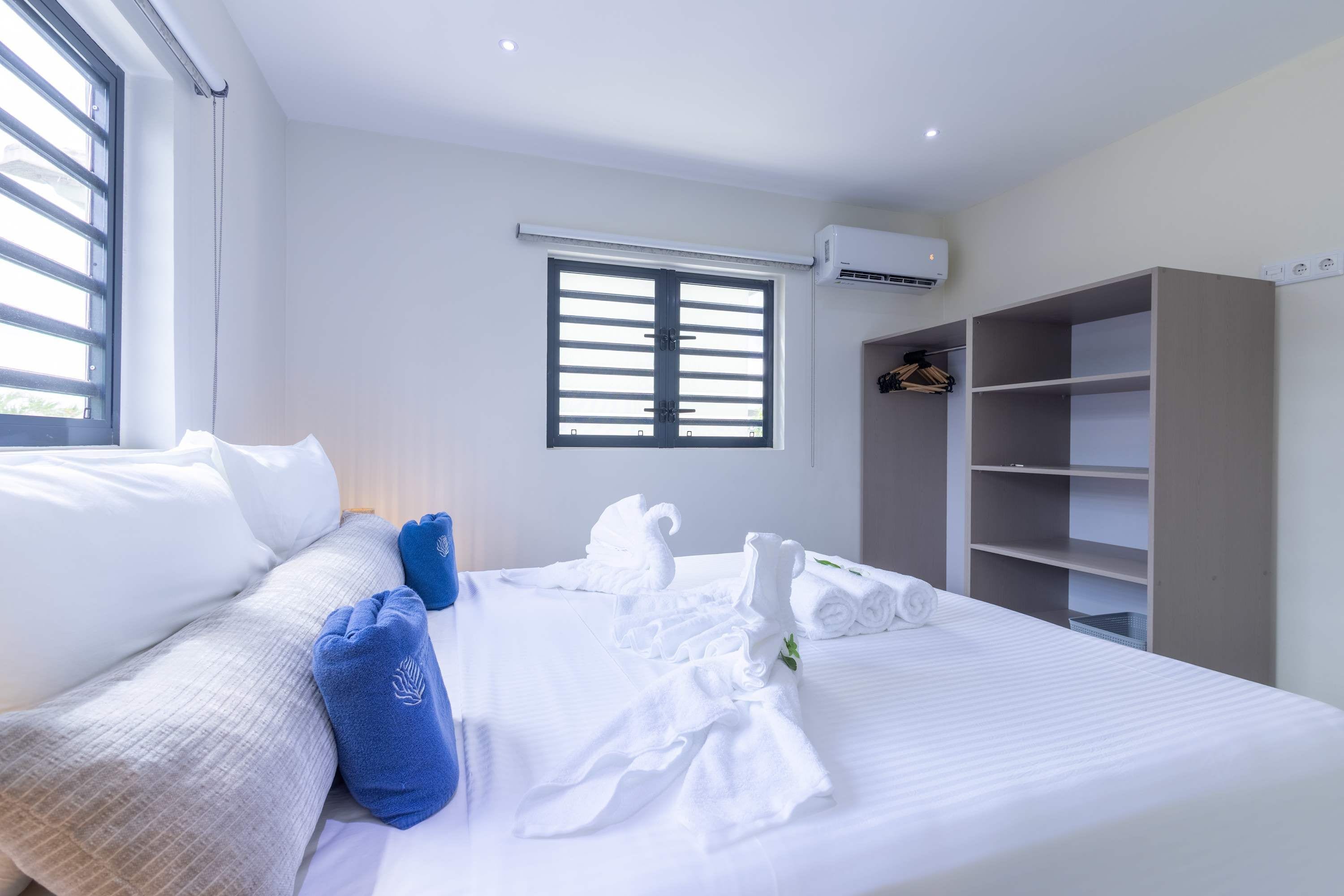 A hotel room with a bed, a wardrobe, a window with blinds, and an air conditioning unit.