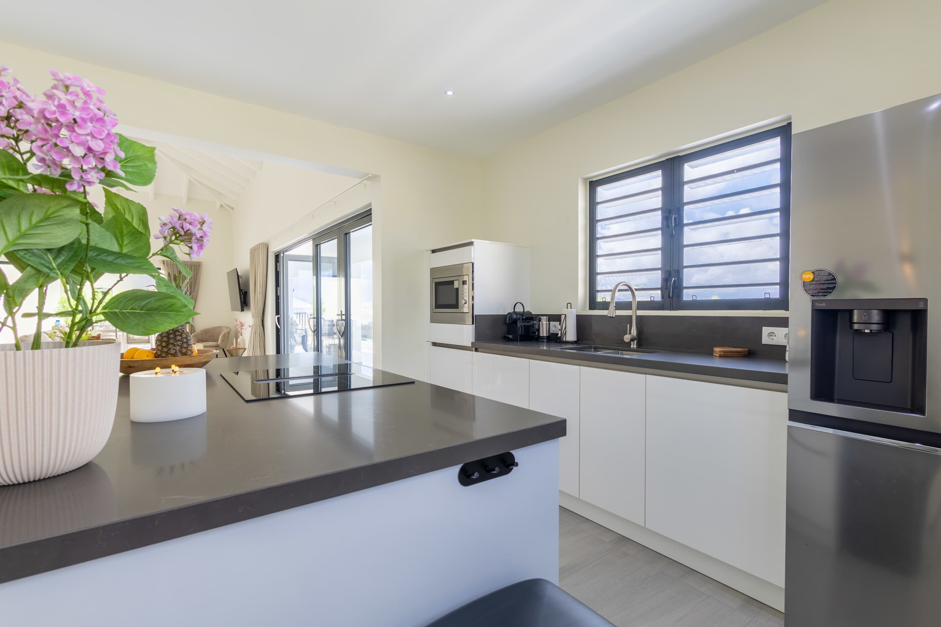 A modern kitchen with a central island, stainless steel appliances, and a window with blinds.