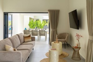 A modern living room with a sofa, a TV mounted on the wall, and a dining area in the background. - Altura Luxury 3BR Penthouse by Mambo Beach (Willemstad)