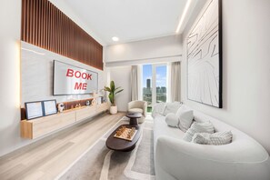A modern living room with a sofa, a coffee table, a TV mounted on the wall, and a large window with a city view. - Stayshort - Amazing 1 Bedroom in Concept 7 JVC Sleeps 2 (Dubai)