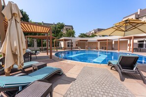 A swimming pool area with lounge chairs and umbrellas. - Stayshort - Gorgeous Studio Apartment in Motor City Sleeps 2 With Balcony (Dubai)