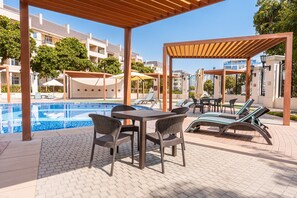 A poolside area with lounge chairs, a table, and umbrellas. - Stayshort - Gorgeous Studio Apartment in Motor City Sleeps 2 With Balcony (Dubai)