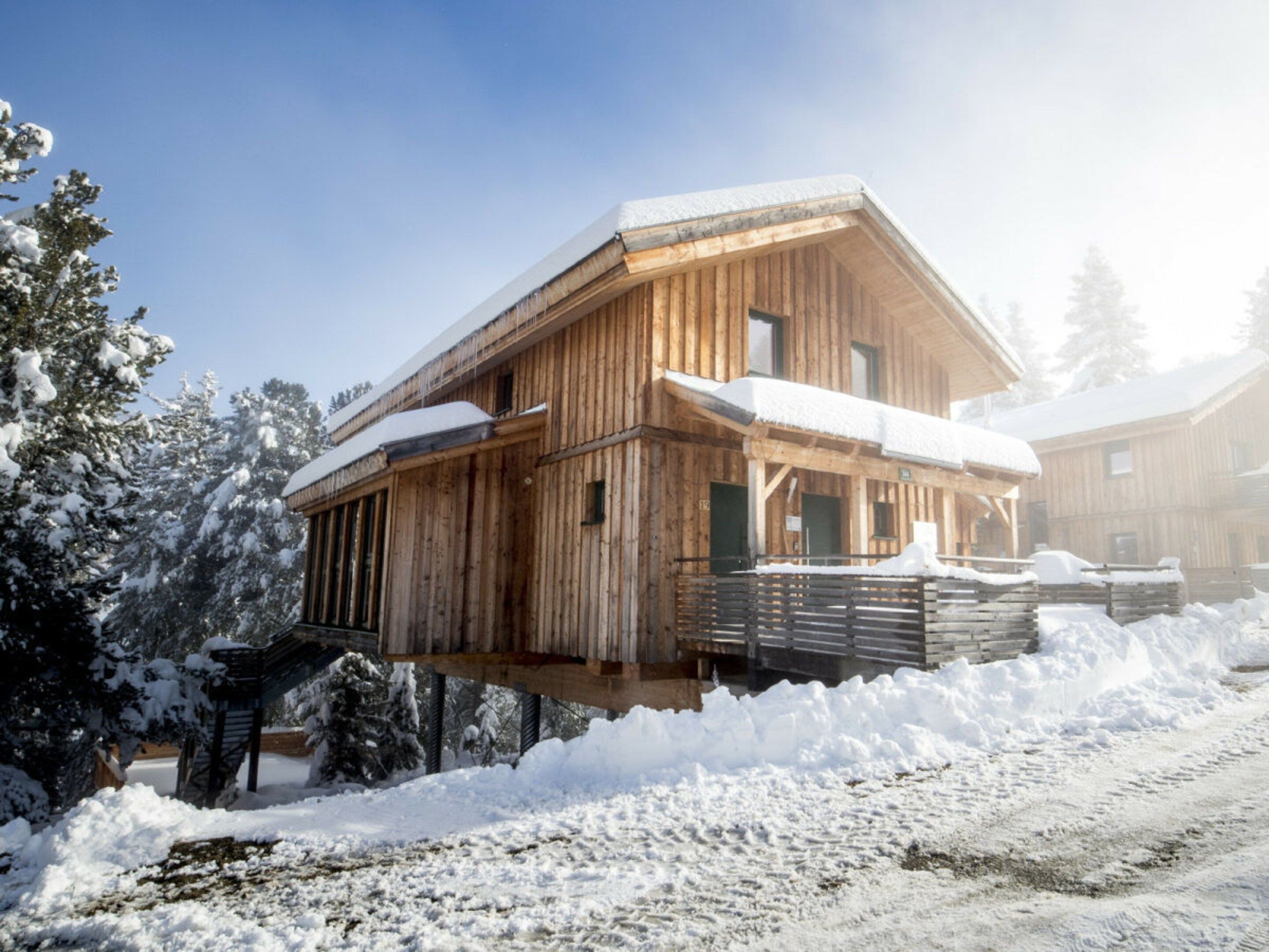 A wooden chalet with a balcony, surrounded by snow-covered trees.