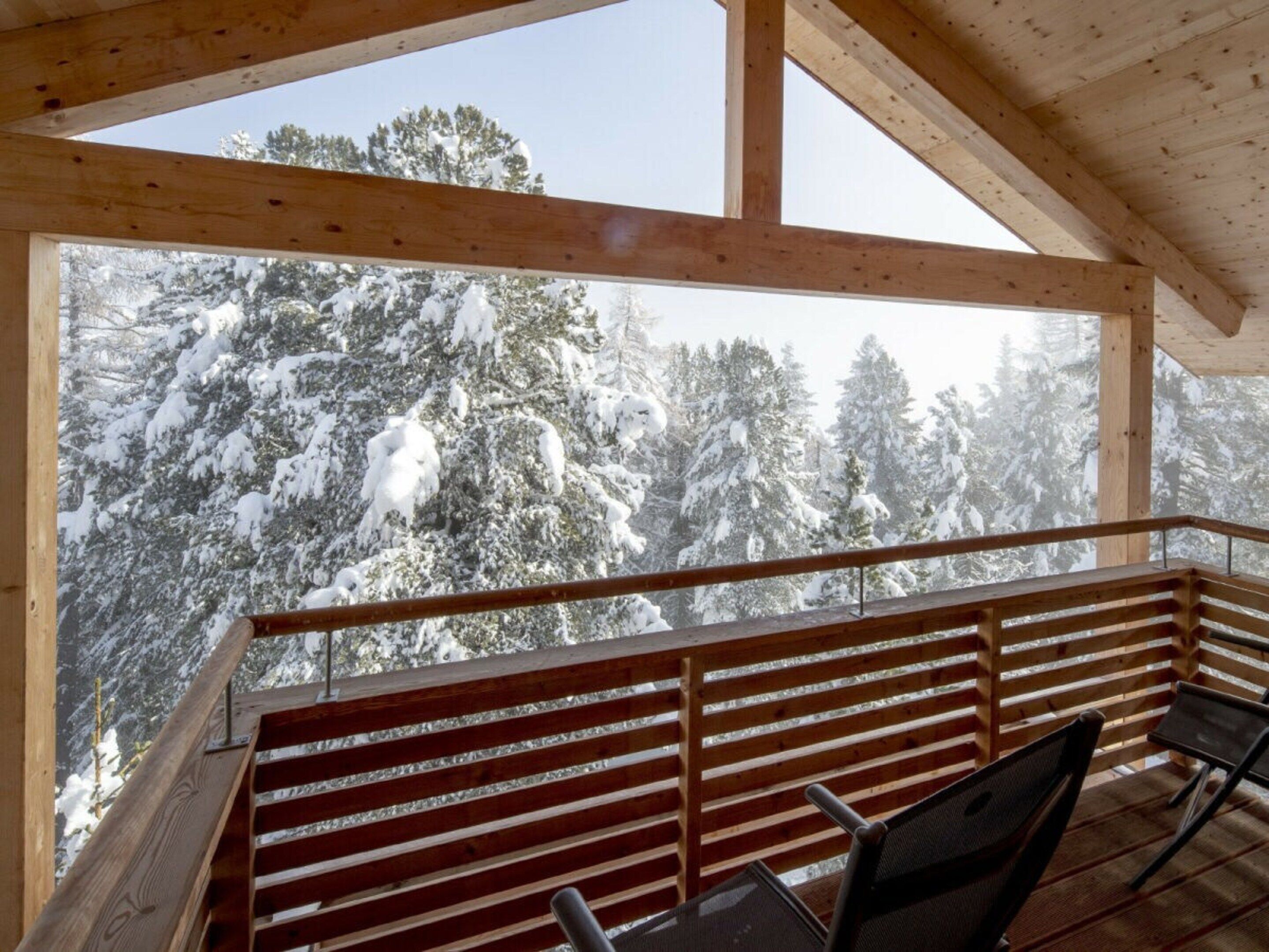 Un balcone in legno con vista su alberi innevati.