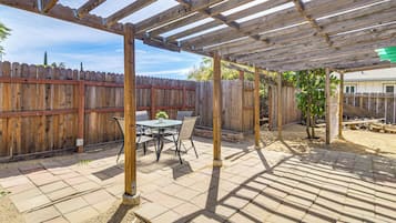 Un patio cubierto con una pérgola de madera, una mesa con sillas y una cerca de madera al fondo.