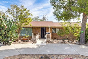 A single-story house with a stone facade, a front porch with a bench, and a small front yard with a cactus and a tree.