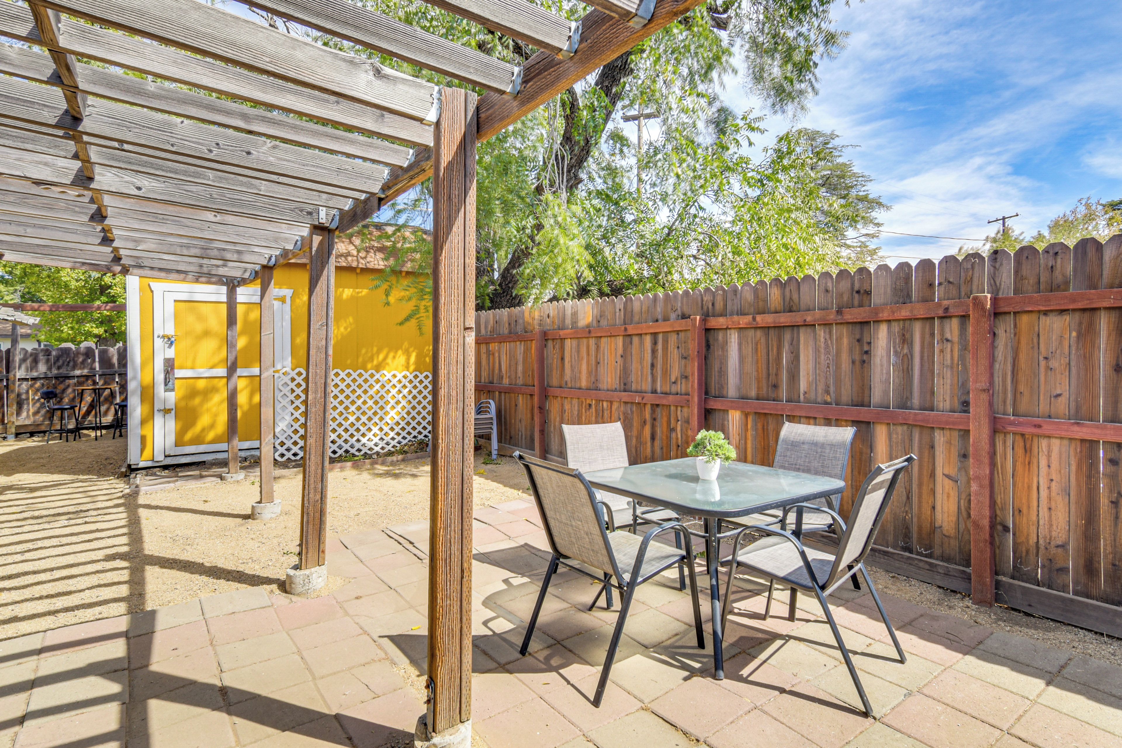 An outdoor patio area with a pergola, a table with chairs, and a wooden fence.